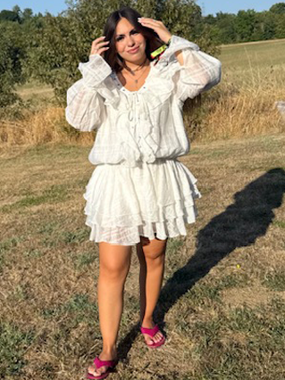 Femme en robe blanche fluide zenoya-paris souriant dans un champ en été près de paris sous un ciel bleu